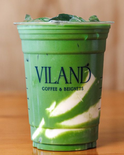 Ly matcha latte đá trong cốc ViLand trong suốt, đặt trên bàn gỗ, phía trên là đá.
